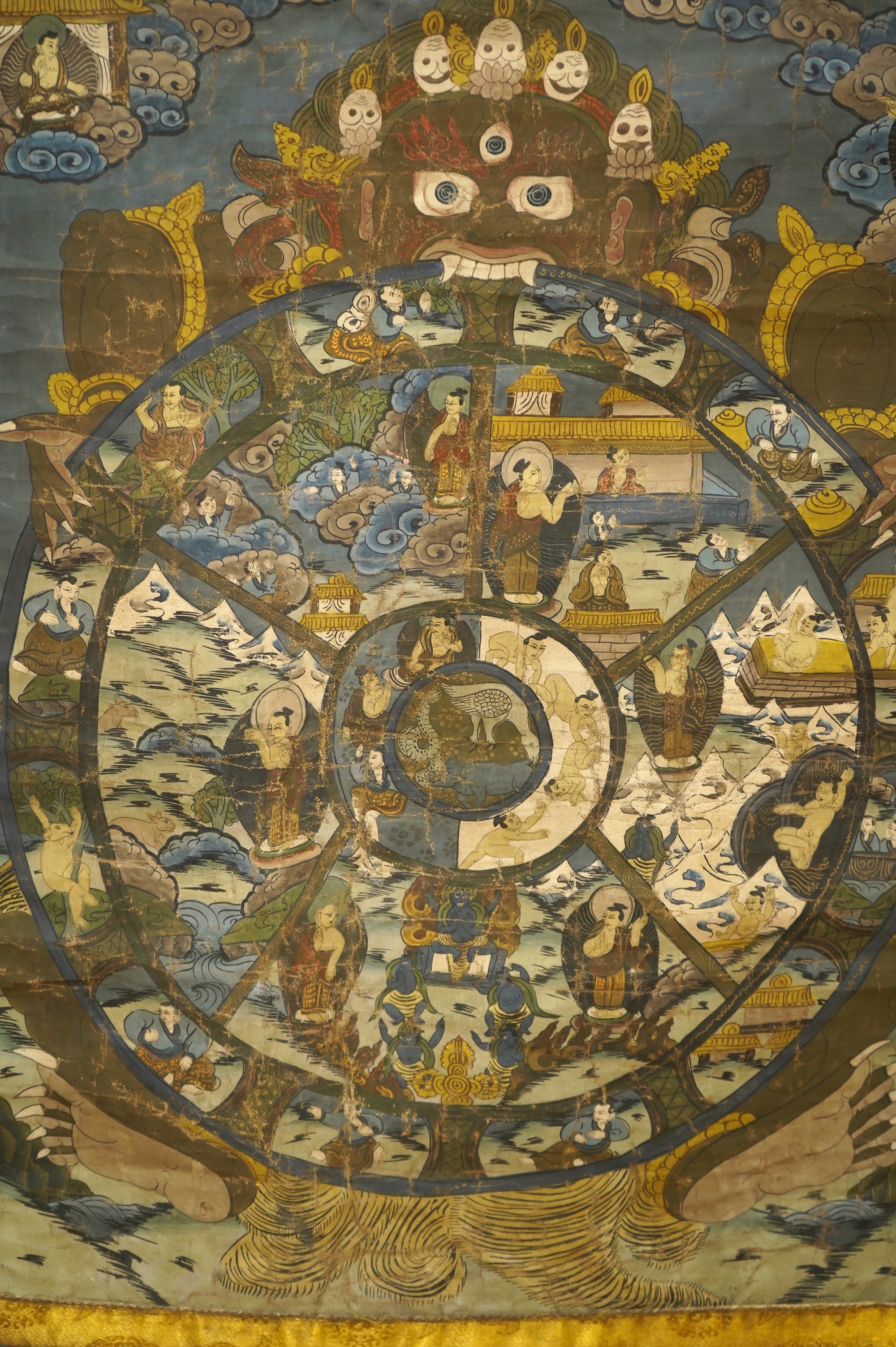 A 20th century Tibetan ‘Wheel of Life’ hand painted damask bordered Thangka, depicting the complex mandala of the circle of existence of beings in Buddhist philosophy, it depicts the teachings of Shakyamuni Buddha, showi